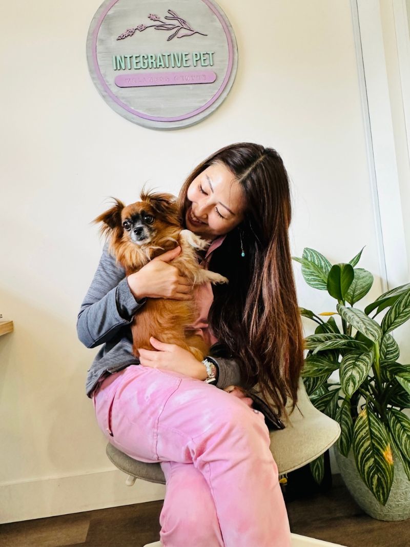 A woman in pink pants holding a small dog.